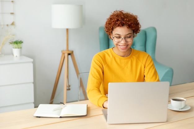 Ragazza afroamericana che usa il computer portatile in ufficio a casa guardando lo schermo digitando in chat leggendo la scrittura