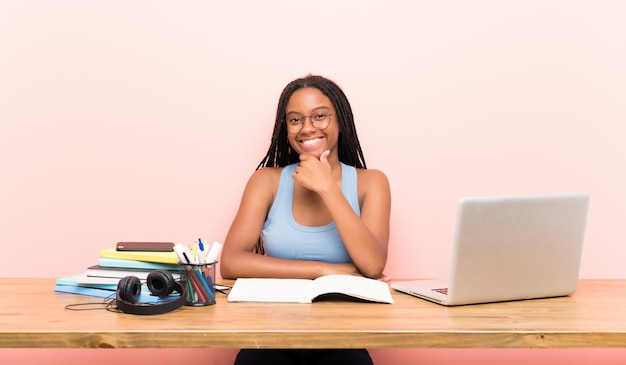 Ragazza afroamericana dello studente dell'adolescente con capelli intrecciati lunghi nel suo luogo di lavoro con i vetri e sorridere