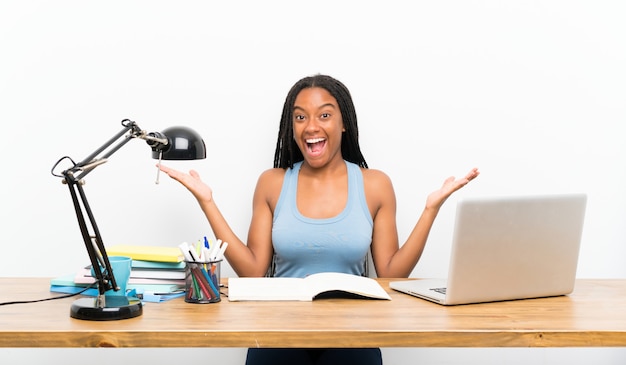 Ragazza afroamericana dello studente dell'adolescente con capelli intrecciati lunghi nel suo posto di lavoro con espressione facciale colpita