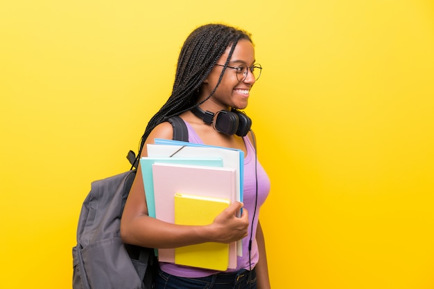 Ragazza afroamericana dello studente dell'adolescente con capelli intrecciati lunghi sopra la parete gialla isolata che guarda al lato