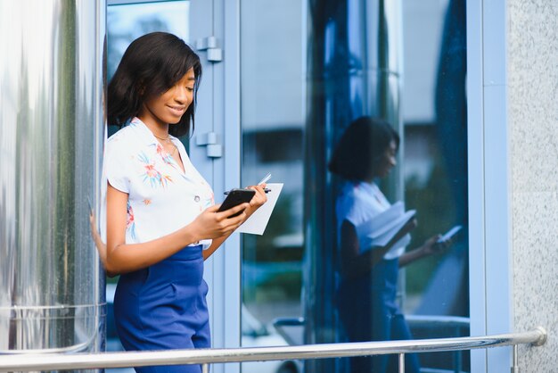 Ragazza afroamericana digitando testo su smart phone in piedi nel mezzo del grande centro business