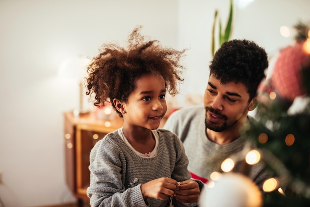 Ragazza afroamericana sveglia che decora un albero di Natale a casa