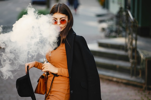 ragazza alla moda che fuma una sigaretta elettronica mentre cammina per la città