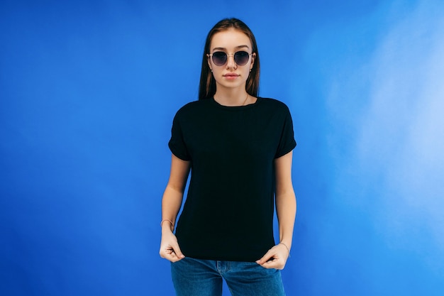 Ragazza alla moda che porta maglietta nera che posa nello studio sullo spazio blu