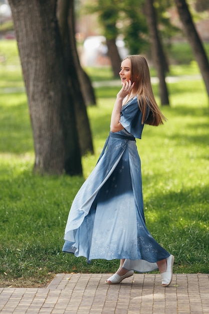 Ragazza alla moda che propone in un vestito in un parco di primavera soleggiata. Ritratto allegro e felice di una bella ragazza in estate.