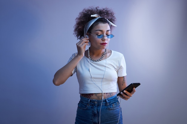 Ragazza alla moda con riccioli afro utilizza uno smartphone e auricolari su uno sfondo blu studio con spazio copia, conversazione online, ascolta musica
