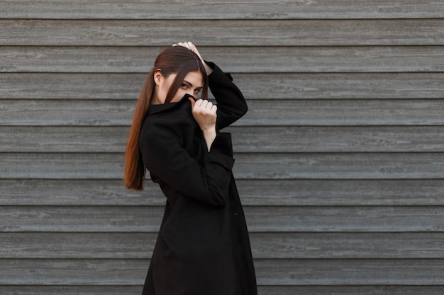 Ragazza alla moda giovane modello in cappotto nero copre il viso