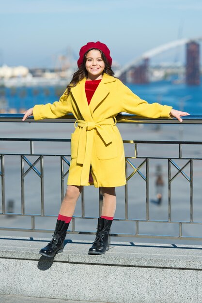 Ragazza alla moda godetevi una passeggiata nella soleggiata giornata primaverile Kid cappello luminoso berretto e cappotto caldo Tendenza in stile francese Spensierata passeggiata rilassata Benefici per la salute di camminare Ragazza adorabile bambino cammina sfondo sfocato