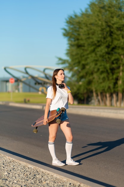 Ragazza alla moda in calze bianche che cammina con il longboard