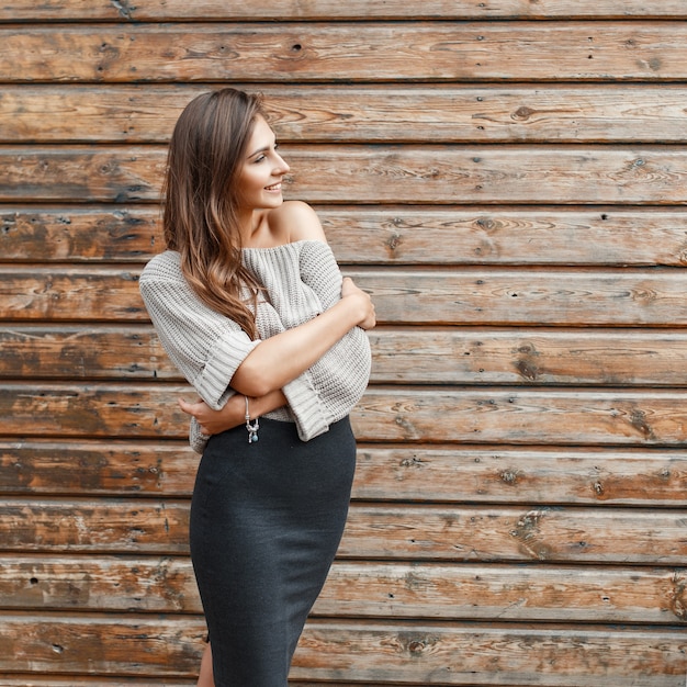 Ragazza alla moda in un maglione grigio e gonna nera vicino alla parete di legno