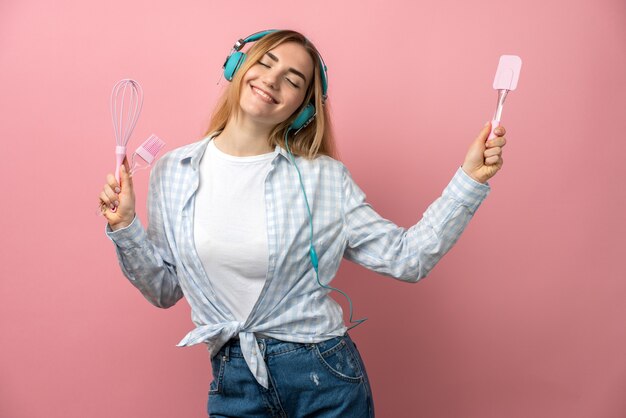 Ragazza allegra ascolta musica e balli in cuffia su uno sfondo rosa