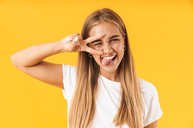 Ragazza allegra che indossa abiti casual in piedi isolata sul muro giallo, mostrando un gesto di pace