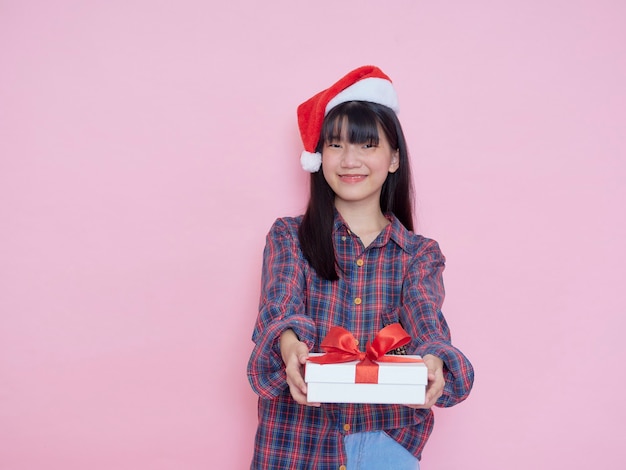 Ragazza allegra che porta il cappello della Santa con i contenitori di regalo della tenuta sulla parete rosa