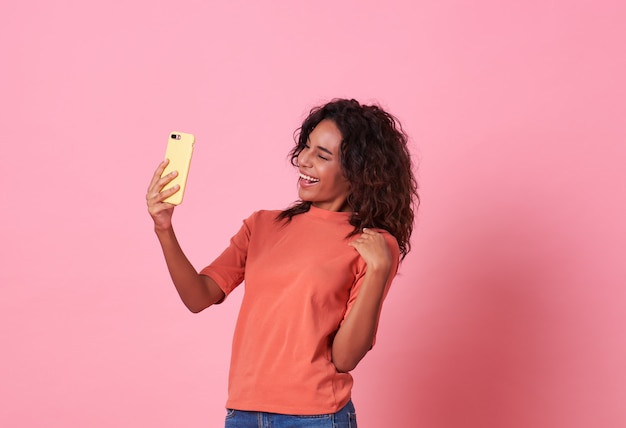 Ragazza allegra che prende un selfie sopra fondo rosa.