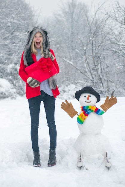 Ragazza allegra che si diverte con il pupazzo di neve nel parco invernale sfondo invernale con fiocchi di neve e pupazzo di neve