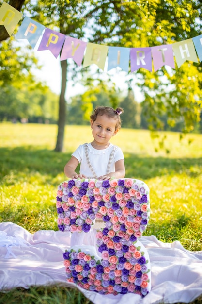 Ragazza allegra che si diverte per il compleanno del bambino su una coperta con decorazioni di carta nel parco