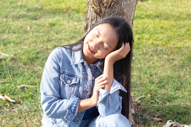 Ragazza allegra che si siede nel parco sorridente e indossa il concetto di stile di vita giacca e jeans