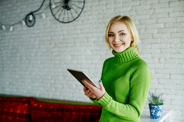 Ragazza allegra con capelli chiari che indossa un maglione verde seduto al caffè con tablet, concetto di freelance, shopping online, ritratto.