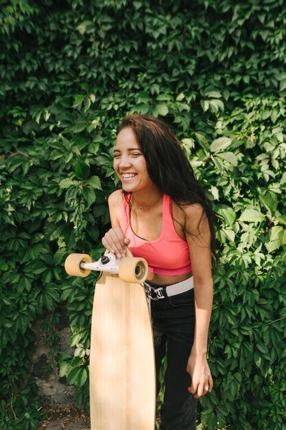 Ragazza allegra con risate longboard su sfondo edera Verticale