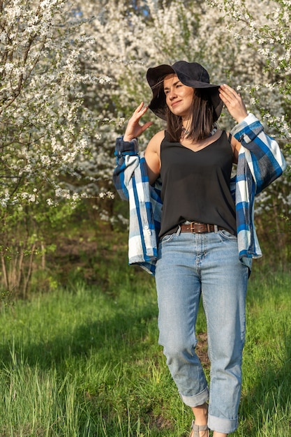 Ragazza allegra con un cappello tra gli alberi in fiore in primavera, in uno stile casual