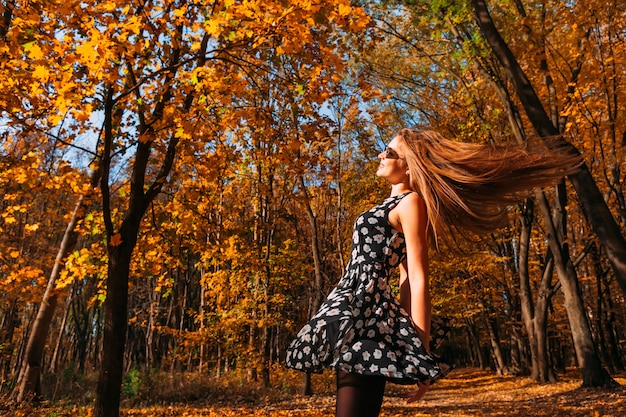 Ragazza allegra e felice dell'adolescente con i capelli lunghi d'ondeggiamento di incandescenza nel volo che fila e che balla nel parco di autunno il giorno soleggiato. Passeggiata nel parco autunnale. Donna felice libera. Spazio per copia.