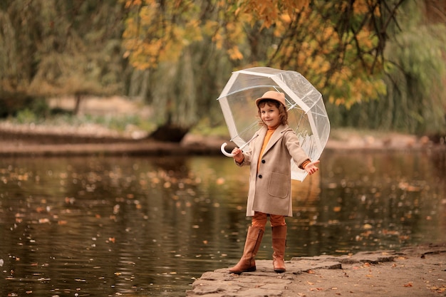 Ragazza allegra felice con un ombrello trasparente su una passeggiata in autunno in riva al lago