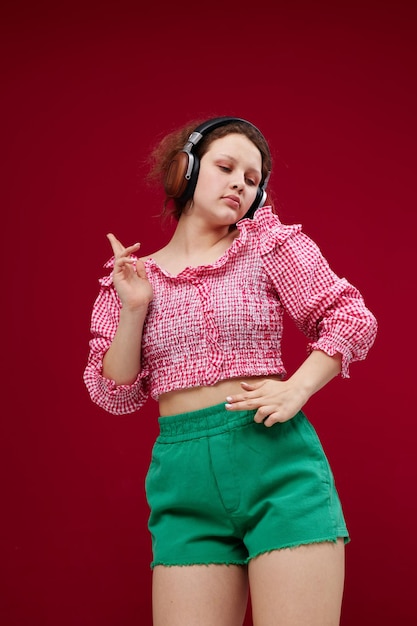 Ragazza allegra in una camicia rosa che ascolta musica in cuffia inalterata