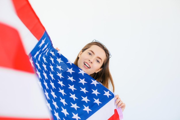 Ragazza americana Felice giovane donna in occhiali da sole a forma di cuore sulla bandiera degli Stati Uniti su sfondo bianco
