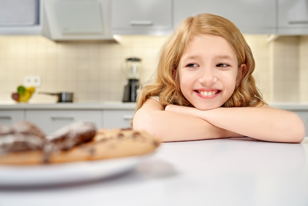 Ragazza appoggiata sul tavolo e guardando gustosi biscotti.