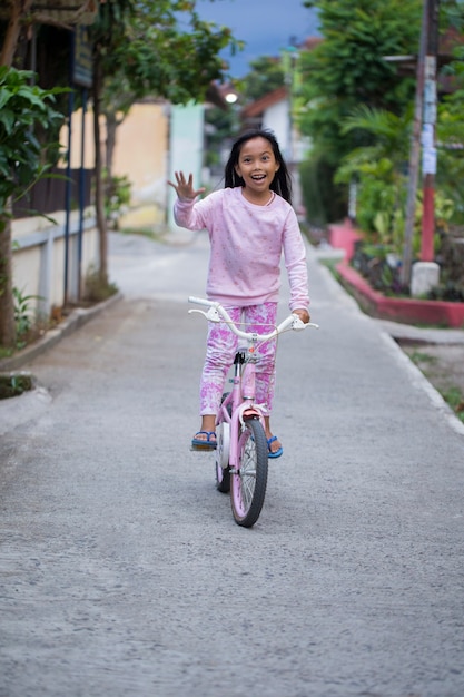 Ragazza asiatica allegra felice del bambino che guida una bicicletta