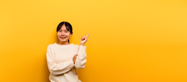 Ragazza asiatica Bella che indossa un abito casual bianco su sfondo giallo. Festeggia la vittoria con un sorriso felice e l'espressione del vincitore con una mano alzata. espressione felice