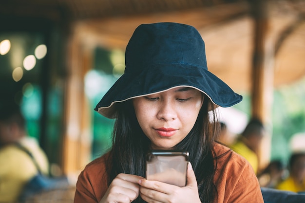Ragazza asiatica che si siede nella caffetteria che gioca il telefono cellulare per i social media in tempo di vacanza, ragazza che si rilassa nella caffetteria per le vacanze, ritratto di ragazza carina.