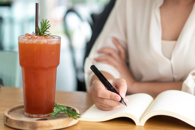 Ragazza asiatica che tiene una penna nera che scrive in un libro vuoto. Diario scrivendo storie