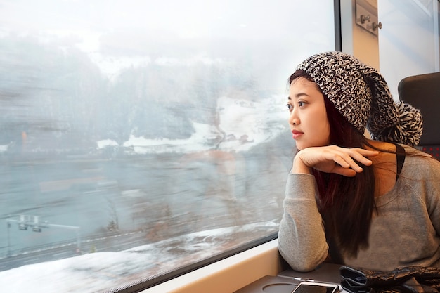 Ragazza asiatica che viaggia in treno e che guarda fuori alla finestra con il lago e fondo della neve nell&#39;inverno.