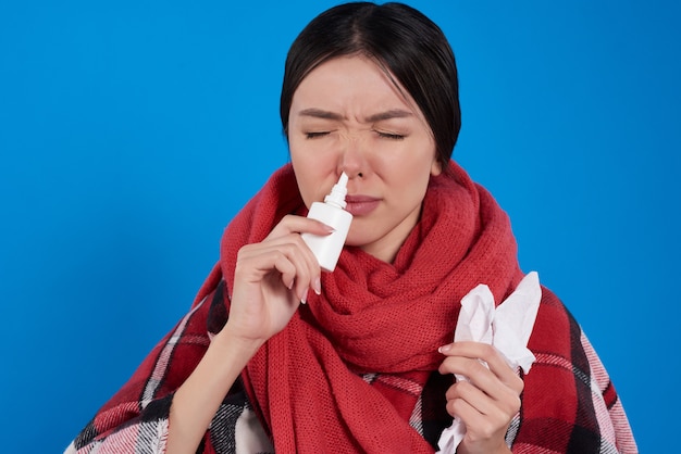 Ragazza asiatica con freddo usando spray nasale isolato