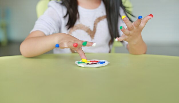 Ragazza asiatica con le dita colorate dipinte nella stanza dei bambini