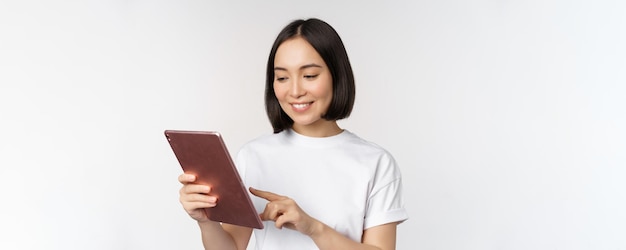 Ragazza asiatica con tavoletta digitale lavorando con gadget shopping online in piedi su sfondo bianco