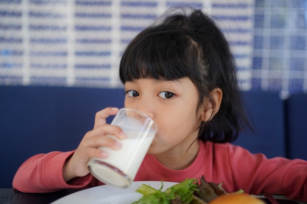 Ragazza asiatica del bambino che beve un bicchiere di latte al mattino. concetto di tempo di colazione.