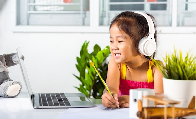 Ragazza asiatica del bambino che studia l'educazione a distanza in videoconferenza a casa