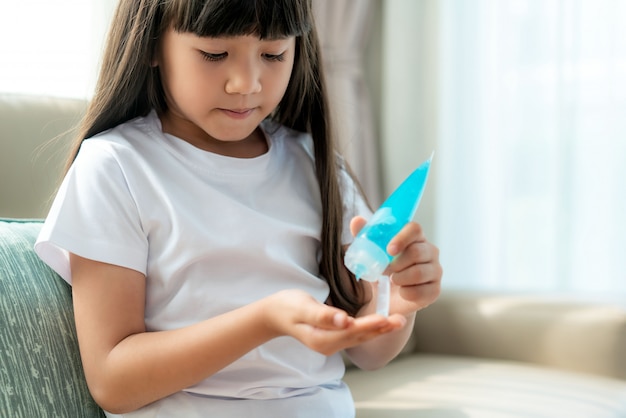 Ragazza asiatica del bambino che usando il gel antisettico dell'alcool