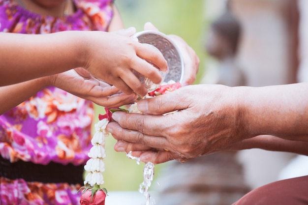 Ragazza asiatica del bambino piccolo che versa acqua sulle mani di anziano anziano o rispettato nonni