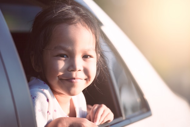 ragazza asiatica del piccolo bambino che sorride e che si diverte a viaggiare in macchina e che osserva fuori dal finestrino di automobile