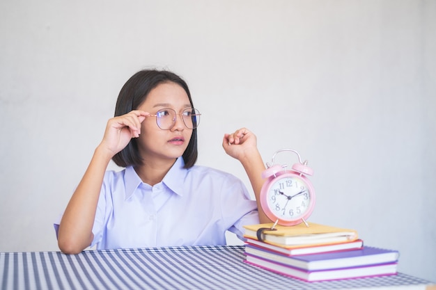 Ragazza asiatica del ritratto che si siede con l'uniforme bianca dello studente di landscapein del libro e