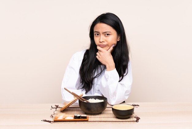 Ragazza asiatica dell'adolescente che mangia alimento asiatico isolato sul pensiero beige