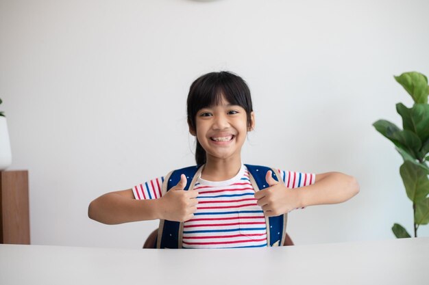 Ragazza asiatica della scuola primaria del bambino con lo zaino che mostra i pollici in su Studente asiatico felice del bambino che celebra il concetto di libertà di ritorno a scuola