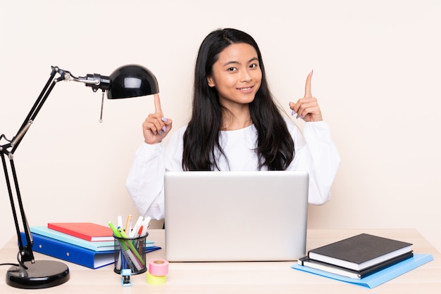 Ragazza asiatica dello studente in un posto di lavoro con un computer portatile isolato su beige