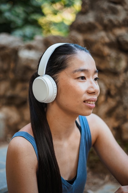 Ragazza asiatica di sport che ascolta la musica sulle cuffie senza fili bianche mentre riposa dalla corsa