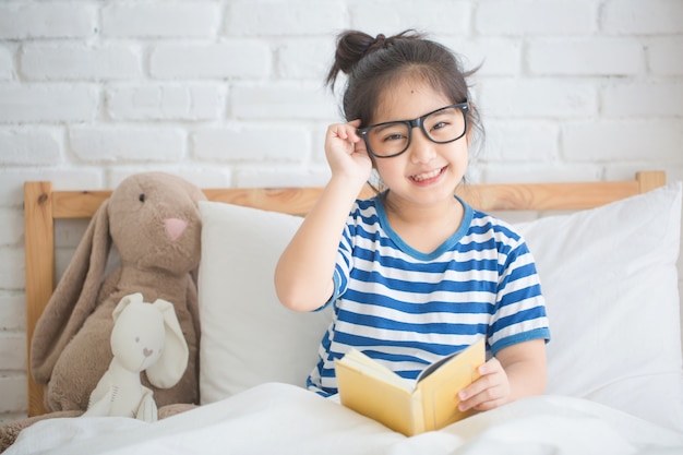 Ragazza asiatica felice che legge il libro di storia sul letto