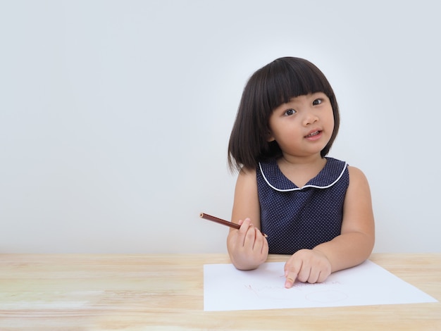 Ragazza asiatica felice del bambino che disegna con la matita colorata.