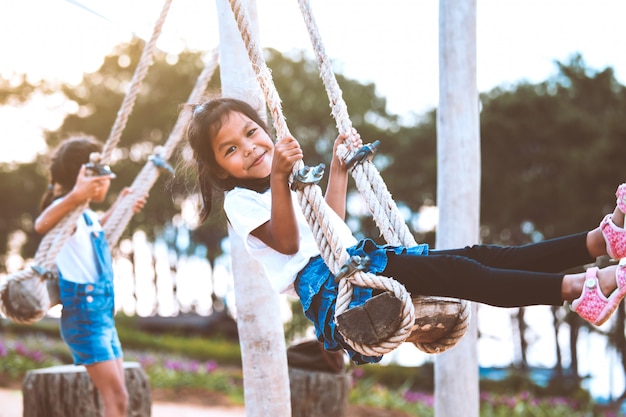 Ragazza asiatica felice del bambino divertendosi per giocare sulle oscillazioni di legno con sua sorella in campo da giuoco